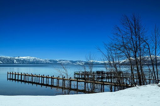 Wide winter view of Lake Tahoe and lakeside piers, with snow covered mountains in background.\n\nTaken from Northshore of Lake Tahoe, California, USA  looking East.