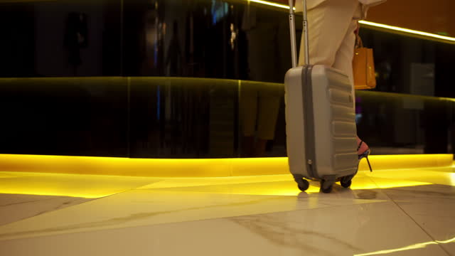 Close-up on the legs of a business woman in high heels dragging her suitcase as she walks towards the reception desk