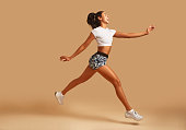 Young athletic woman in sportswear running in front of brown background.