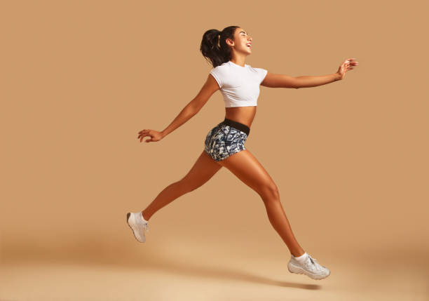 young athletic woman in sportswear running in front of brown background. - running women jogging profile imagens e fotografias de stock