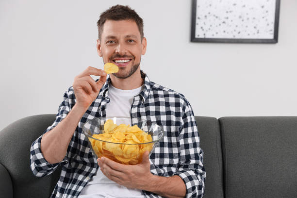 istock Handsome man eating potato chips on sofa at home 1483392390