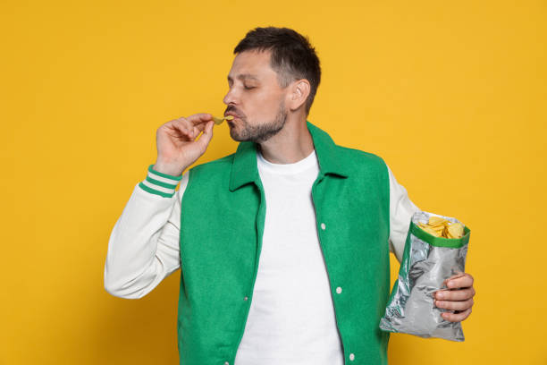 istock Handsome man eating potato chips on orange background 1483392427