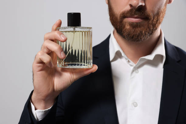 istock Handsome bearded man with bottle of perfume on light grey background, closeup 1483392904