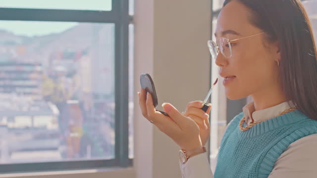 Makeup, lipstick and mirror with an asian woman in her home to apply a cosmetic product for beauty. Face, cosmetics and lifestyle with an attractive young female applying color to her lips or mouth