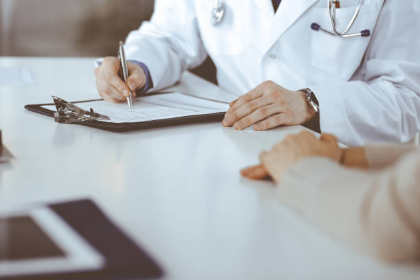 istock Unknown male doctor and patient woman discussing something while sitting in clinic and using clipboard. Best medical service in hospital, medicine, pandemic stop 1483407776