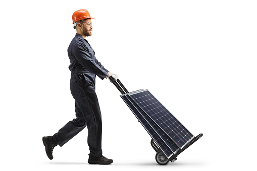 Full length profile shot of a factory worker pushing hand truck with solar panels isolated on white background