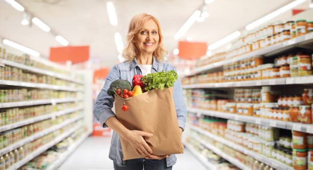 mature woman carrying a paper bag with groceries in a supermarket - sale stok fotoğraflar ve resimler