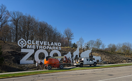 Cleveland, OH, USA - April 13, 2023: Workers finish the installation of a new sign for the Cleveland Metroparks Zoo. The sign faces a major freeway and can be seen by motorists passing by.