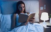Young woman reading book in bed at night