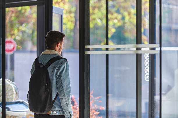After finishing his work, a man steps out of his office while carrying a backpack and wearing wireless headphones, ready to unwind and enjoy the freedom of the urban environment, suggesting a modern approach to work and personal life.