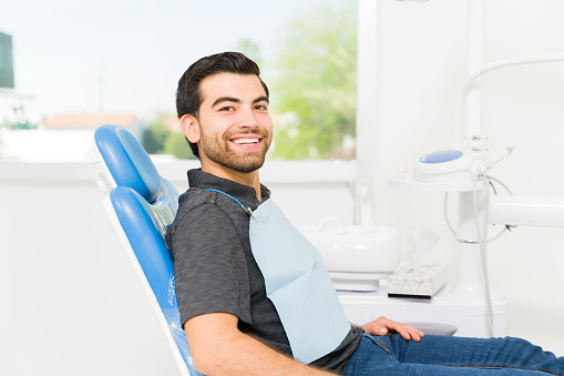 Portrait of latin young man and patient smiling at the dentist and looking happy after a whitening treatment