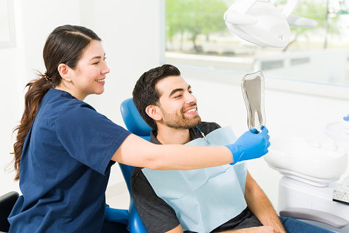 Excited male patient looking at his teeth in the mirror and smiling after doing a whitening or dental treatment at the dentist