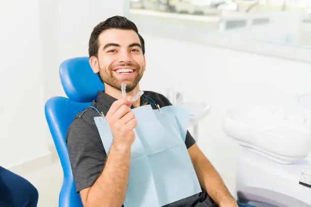 Cheerful attractive young man smiling looking happy with te results of his invisible orthodontics at the dentist