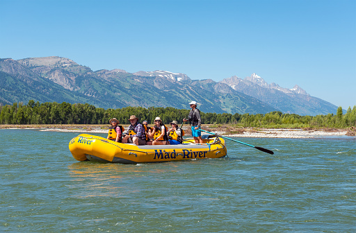 Tourists in rigid inflatable boat on Snake River scenic rafting with Grand Teton mountain range, Wyoming, USA.