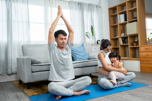 famille heureuse, parents et enfants. se détendre en faisant une posture de yoga avec les bras levés vers la tête. le fils et la fille suivent leurs parents avec bonheur. femme enceinte ventre enceinte près de la naissance - torso physical therapy patient relaxation exercise photos et images de collection