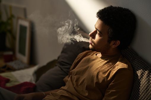Young man in melancholy smoking and thinking about his problems alone sitting in the room