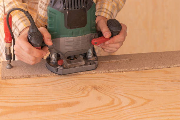 istock Crop anonymous male carpenter using electric milling machine while cutting wood plank in home workshop 1483467497