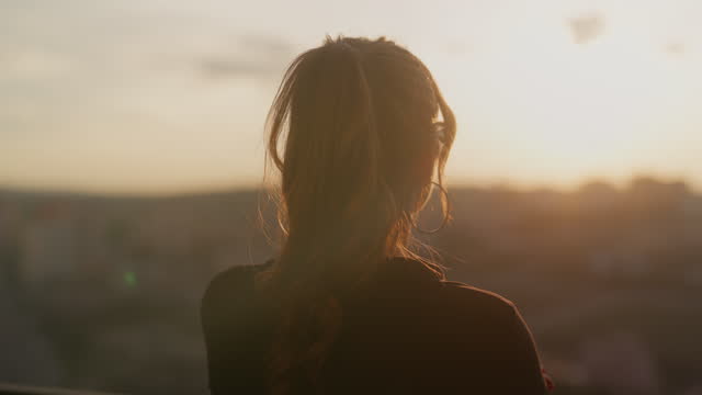 Young woman standing at balcony and watching sunset