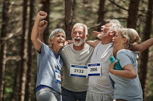 Cheerful seniors having fun while holding their hands high up and celebrating the end of successful marathon race in nature.