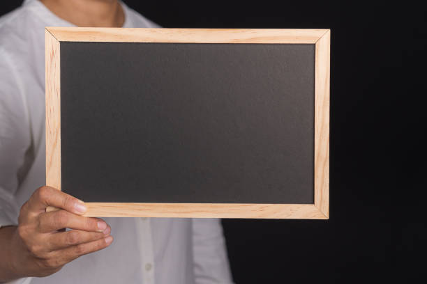 istock Hand of a man holding a small blackboard while standing on a black background. 1483472599