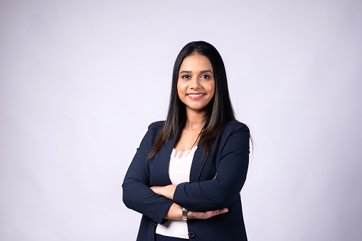 Smiling Indian young woman professional wearing formal dress with arms crossed and looking at camera isolated on grey blank studio background ,copy space.