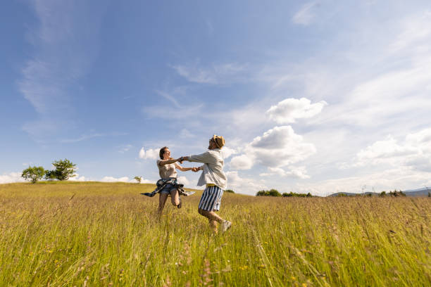 Happy couple having fun while holding hands and spinning during a spring day in nature. Copy space.