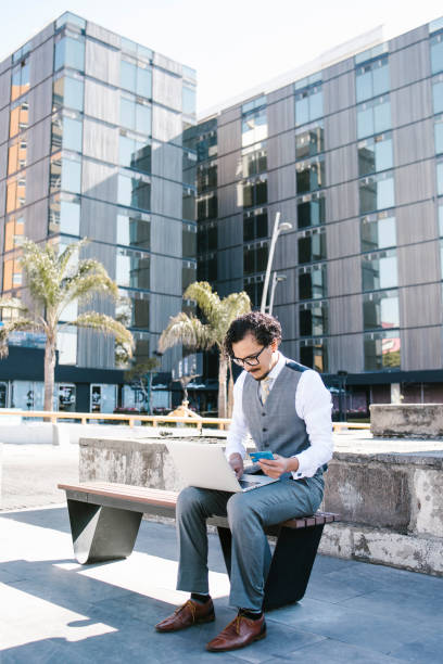 istock young latin businessman using laptop and phone working on computer in bench outdoors in Mexico city, Latin America hispanic people 1483480010