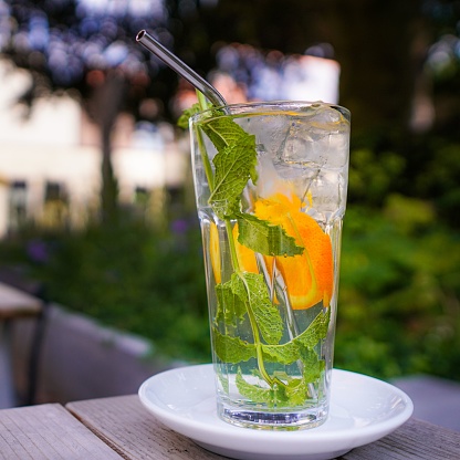 A close-up shot of an ice-cold beverage with mint and orange slices in an outdoor setting