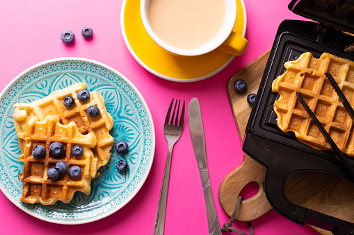 morning and bright breakfast on the pink background. belgian waffles with blueberries and coffee