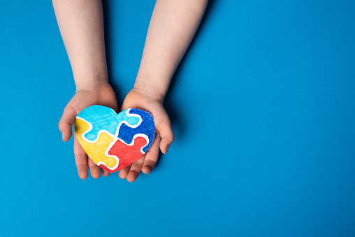 Child hands holding a puzzle heart on a blue background