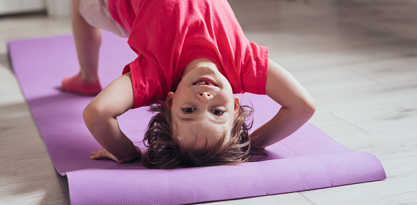 Child stands on his head on the mat to do the exercise. The concept of health, sports, learning online. Copy space, banner