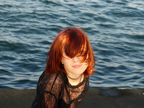 portrait of a smiling red-haired teenage girl against the backdrop of the sea.