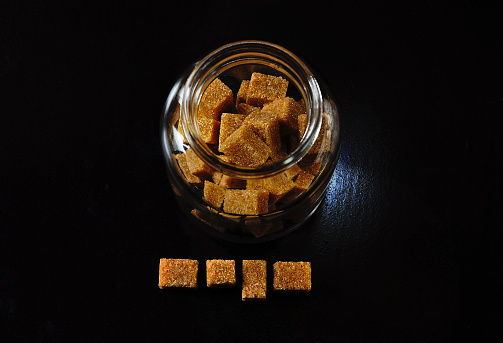 Directly above shot of brown sugar cubes in glass jar on dark background