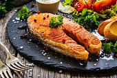 Fried salmon steak, toasted bread and fresh vegetables on black wooden background