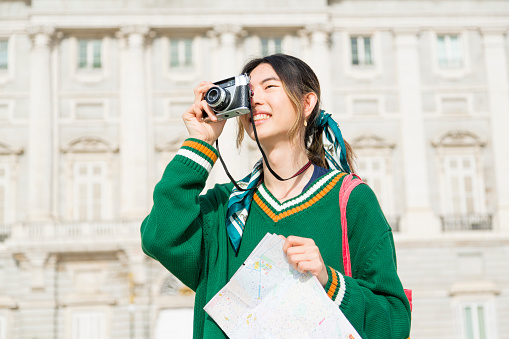 Young Asian traveler exploring the city with a map and camera, capturing memories and discovering new experiences