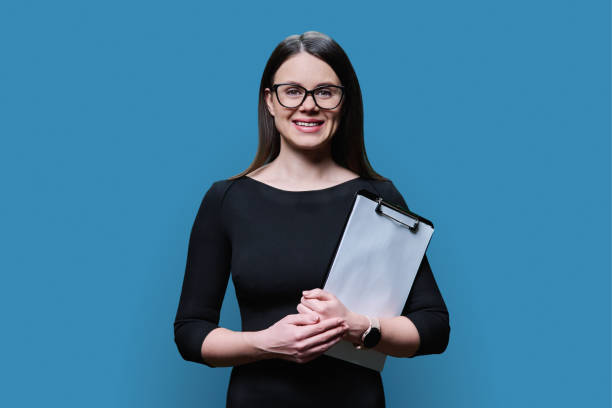 istock Young woman with clipboard looking at camera on blue background 1483493643