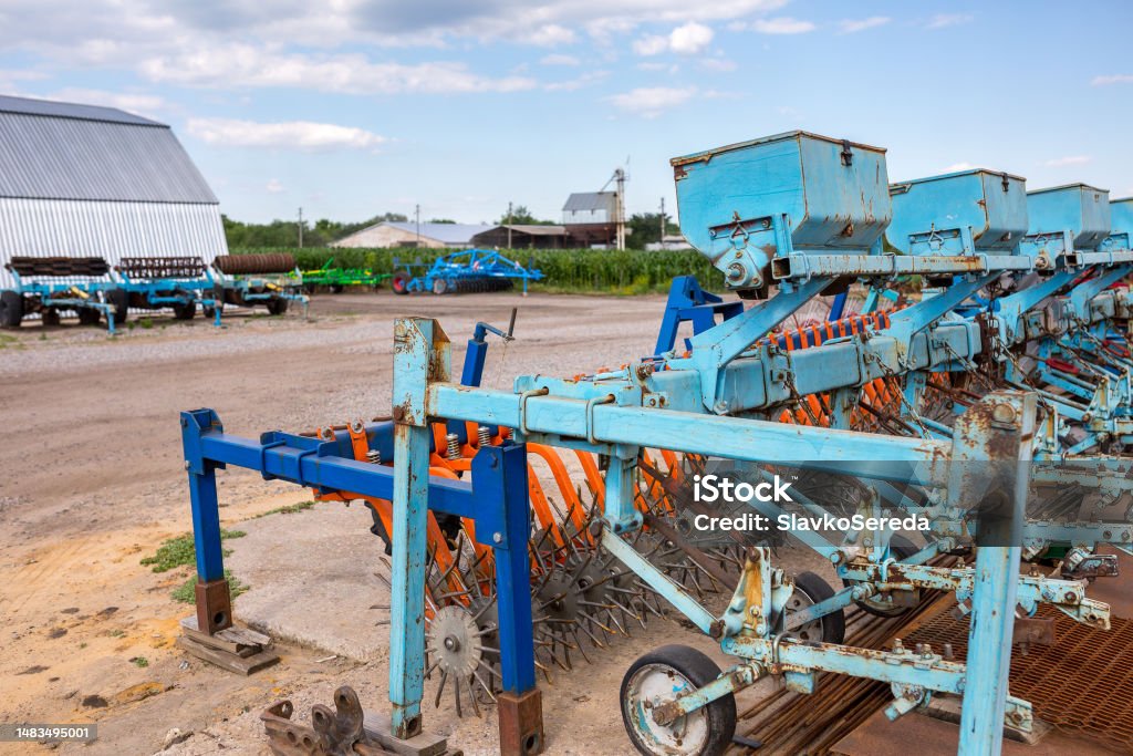 Old trailed seeder are standing near the arches hangar on the material and technical base of the agricultural enterprise. Farm enterprise in central region of Ukraine. Agricultural Field Stock Photo