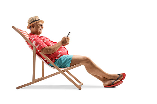 Mature male tourist sitting on a beach chair with a smartphone isolated on white background