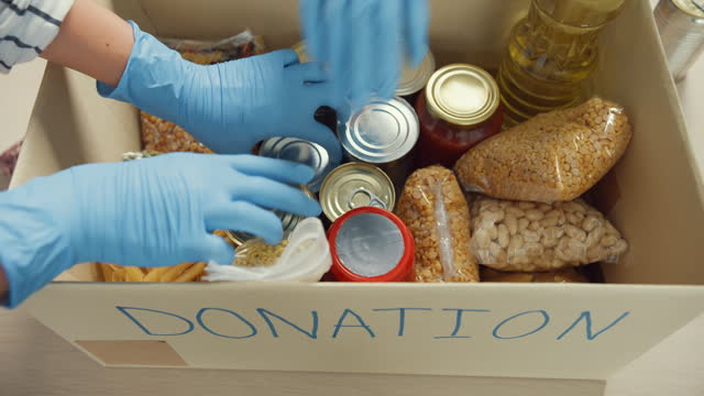 Group of young Asia teenage girl volunteer wear gloves packing food and drink donation into donations paper boxes while work in charitable foundation. Social worker, food bank and coronavirus.