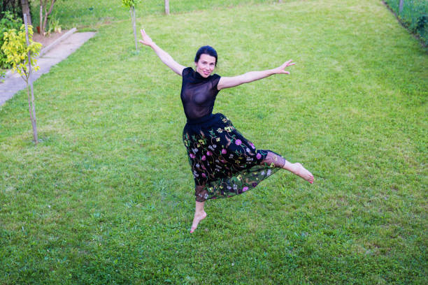 A young attractive woman in black clothes dancing in a backyard