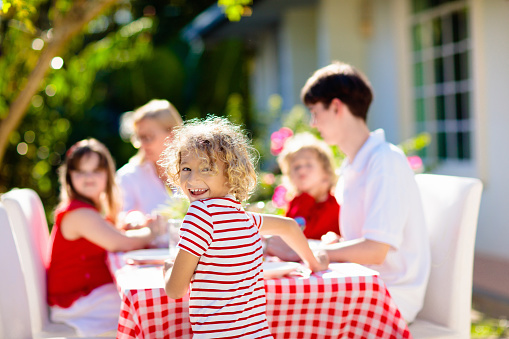 Family eating outdoors. Garden summer fun. Barbecue in sunny backyard. Grandmother and kids eat lunch in outdoor deck. Parents and children enjoy bbq. Boy and girl with mother.