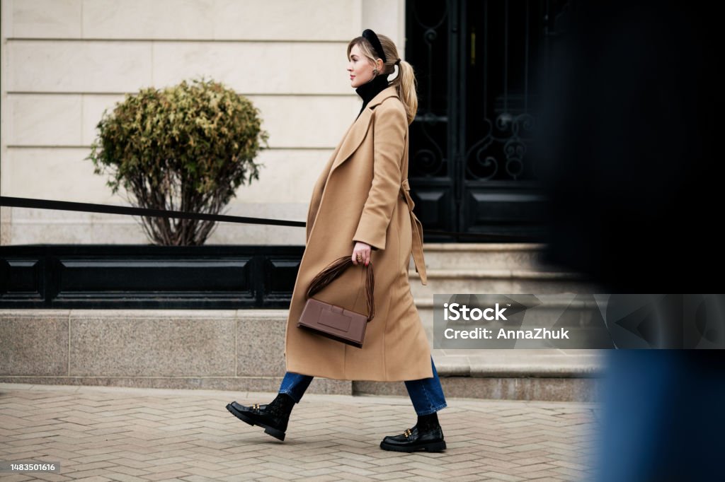 Side view beautiful woman walking street in fashionable spring or autumn clothes cashmere coat, jeans, loafers shoes and small bag. Full length Female model in motion, street style fashion Women Stock Photo