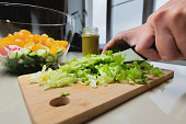 The cook cuts the salad with a knife on the table at home. The process of cutting and cooking food in the kitchen close-up