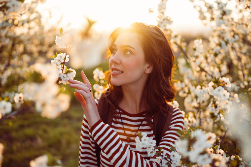 Beautiful young woman enjoying carefree spring day in blossoming orchard.
