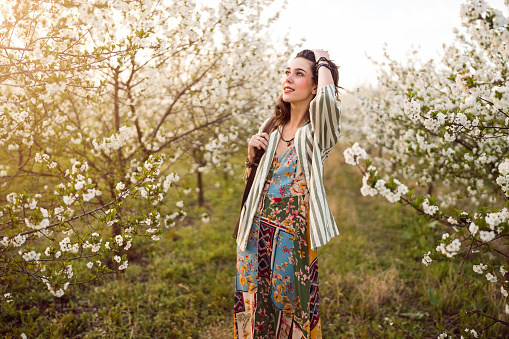 Beautiful young woman walking through blossoming orchard in spring.