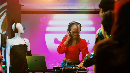 Happy DJ woman mixing sounds on station, wearing headset and using audio panel equipment at discotheque. Smiling person having fun with electronic live music on clubbing stage.