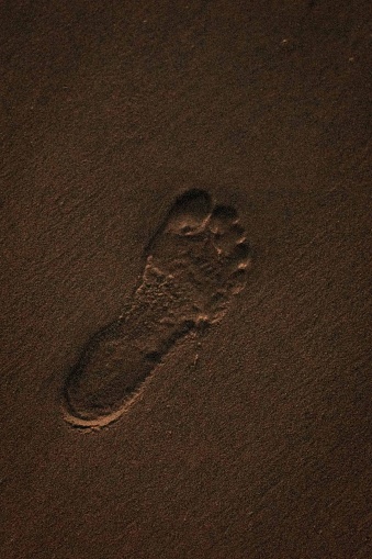 A close-up shot of a single human footprint in the sand