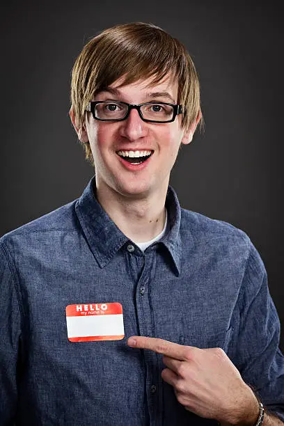 A studio headshot of a young man pointing at a blank nametag.