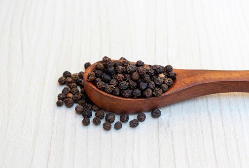 Black Pepper in a Wooden Spoon Isolated on White Wooden Background.