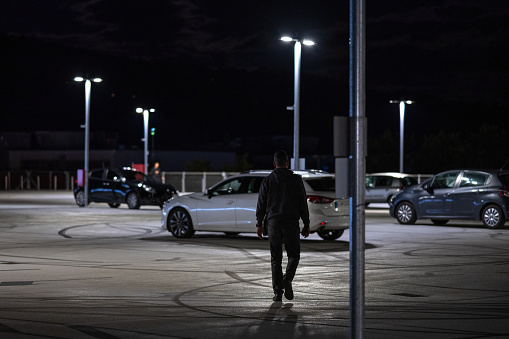 Man walking in outdoors car parking space at night.